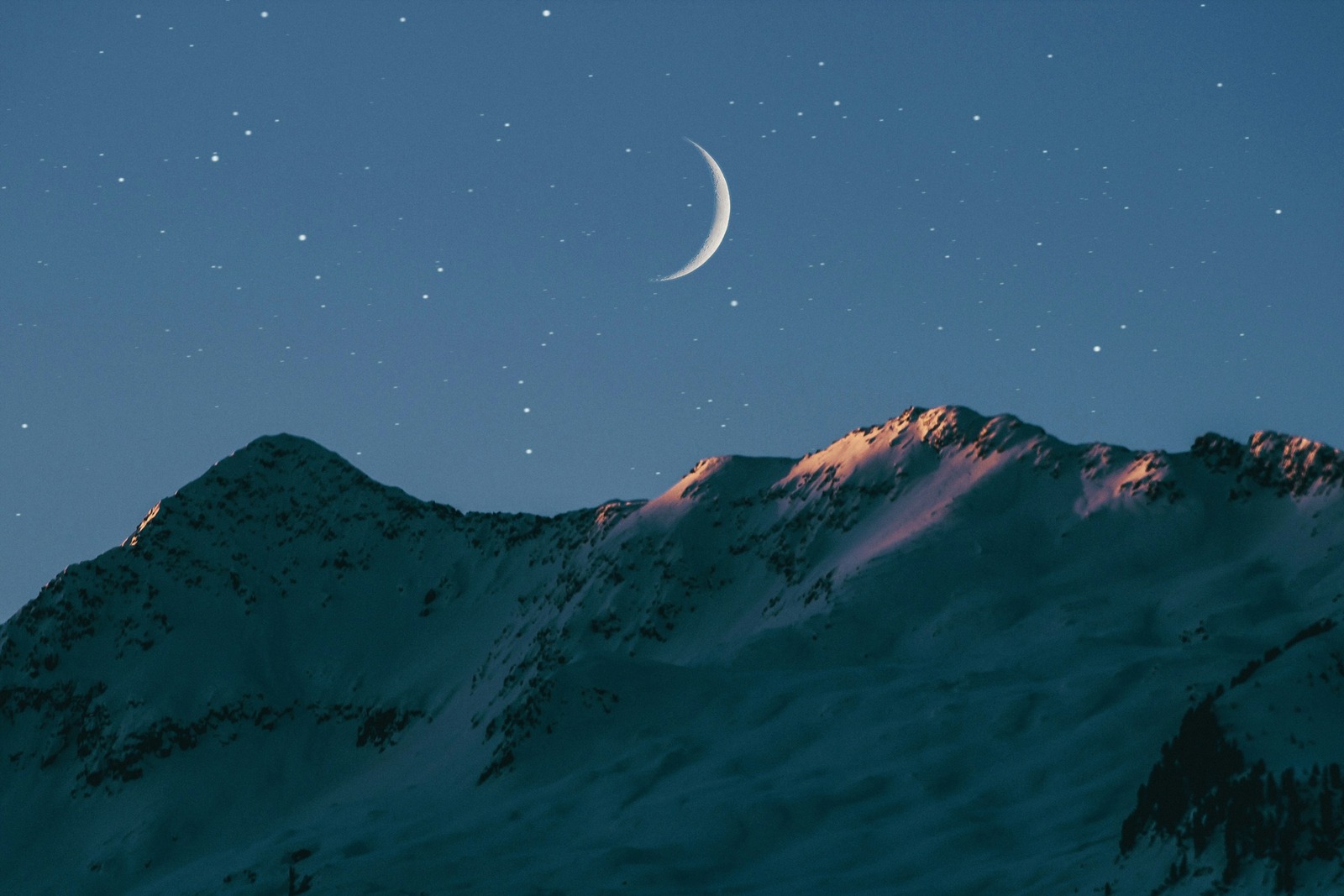 Fin croissant de lune apparaissant au-dessus des reliefs à la tombée de la nuit